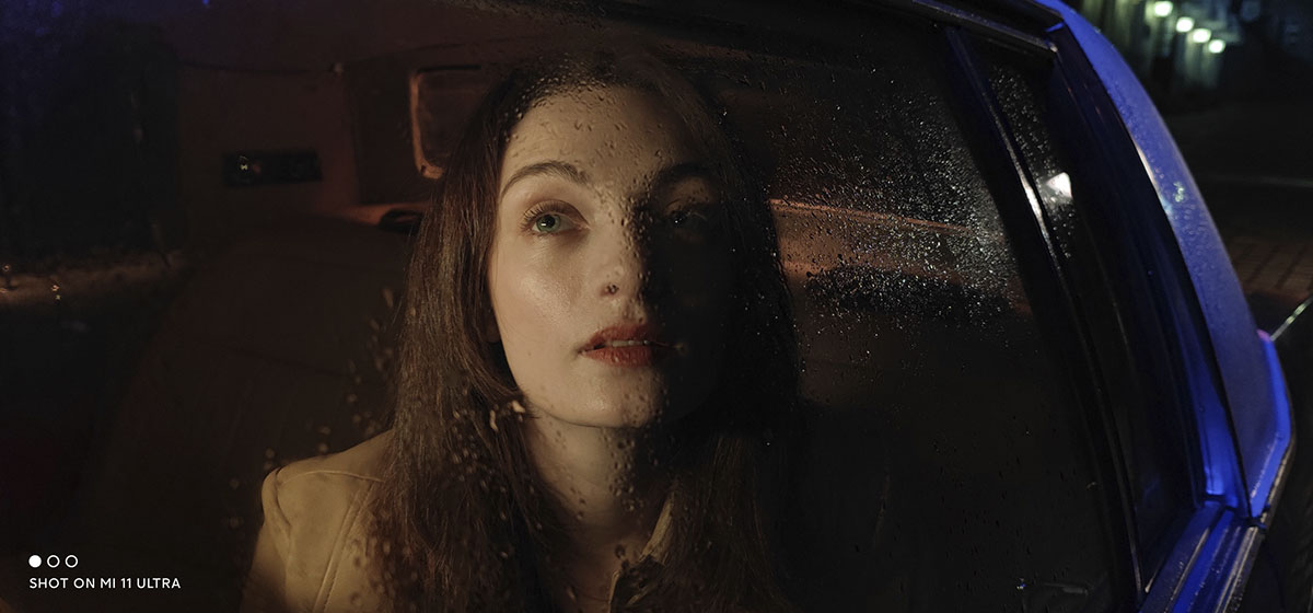 Donna in automobile, ritratta attraverso il vetro bagnato di gocce di pioggia.