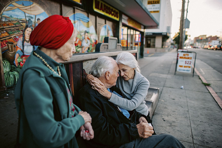 Jeanie abbraccia Will alla fermata dell'autobus, mentre Adina è in piedi accanto a loro, Los Angeles, California. © Isadora Kosofsky