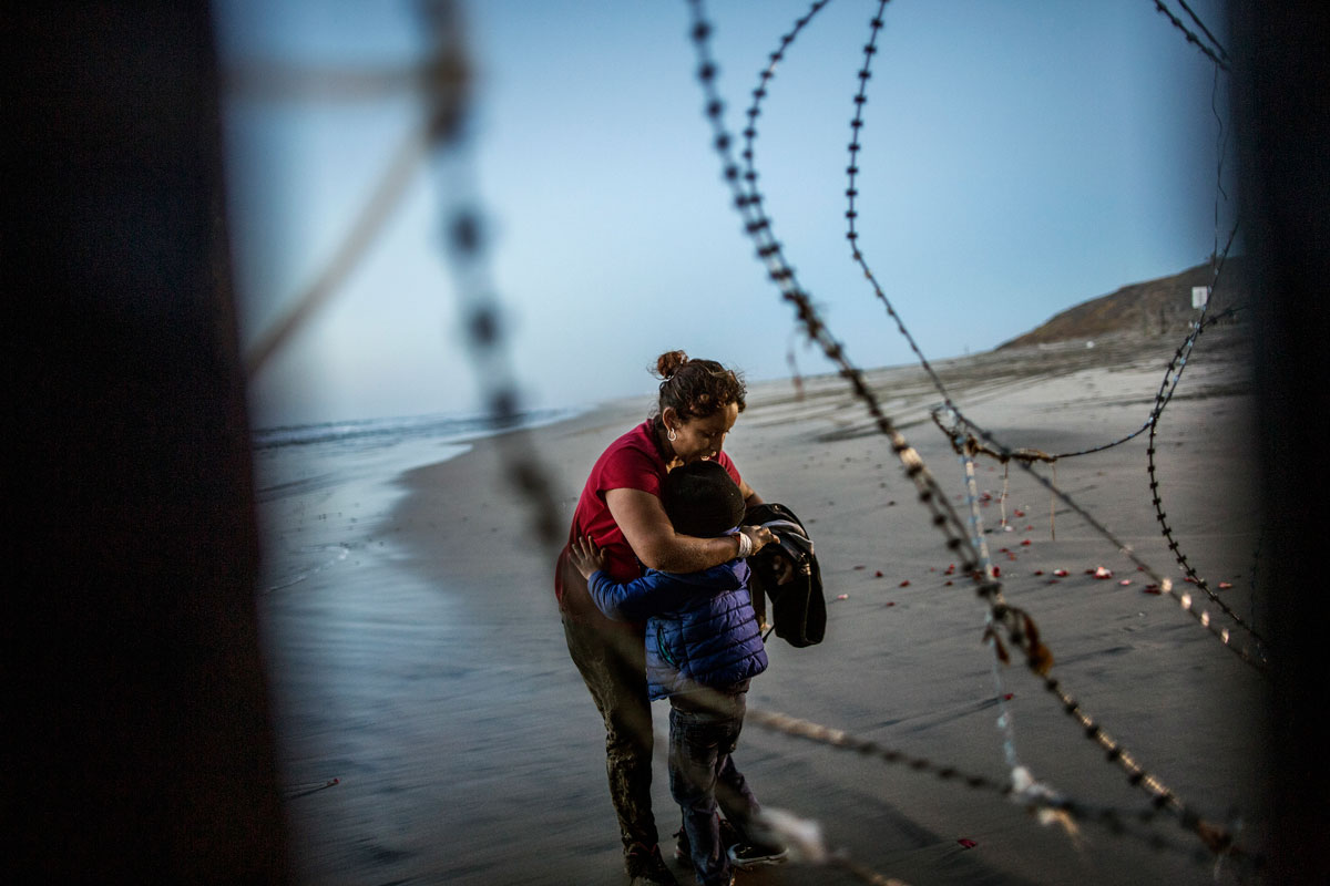 Una donna migrante dell'America centrale abbraccia il suo bambino dopo aver attraversato il muro di confine tra Messico e Stati Uniti presso la spiaggia di Tijuana, in Messico, il 14 dicembre 2018. © Fabio Bucciarelli