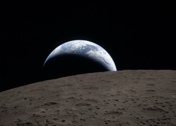 Tramonto della Terra ripreso attraverso il finestrino della navicella Orion alle 18:41 EDT del 6 aprile 2026, durante il sorvolo della Luna da parte dell’equipaggio di Artemis II. Una Terra di un blu attenuato, solcata da nubi bianche luminose, tramonta dietro la superficie lunare punteggiata di crateri. La parte in ombra della Terra è immersa nella notte. Sul lato illuminato del pianeta si distinguono nubi in movimento sopra la regione di Australia e Oceania. In primo piano, il cratere Ohm mostra bordi terrazzati e un fondo piatto interrotto da picchi centrali. I picchi centrali si formano nei crateri complessi quando la superficie lunare, liquefatta dall’impatto, risale verso l’alto durante la formazione del cratere. © Photo Credits: NASA