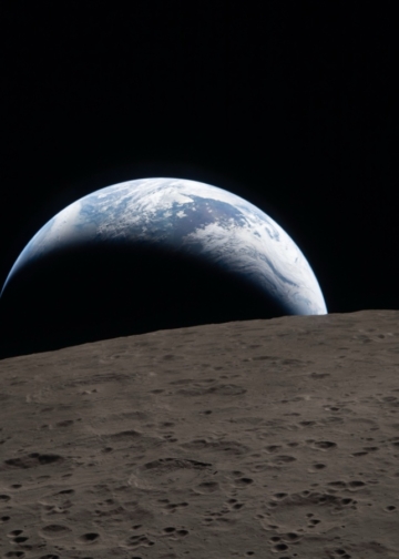 Tramonto della Terra ripreso attraverso il finestrino della navicella Orion alle 18:41 EDT del 6 aprile 2026, durante il sorvolo della Luna da parte dell’equipaggio di Artemis II. Una Terra di un blu attenuato, solcata da nubi bianche luminose, tramonta dietro la superficie lunare punteggiata di crateri. La parte in ombra della Terra è immersa nella notte. Sul lato illuminato del pianeta si distinguono nubi in movimento sopra la regione di Australia e Oceania. In primo piano, il cratere Ohm mostra bordi terrazzati e un fondo piatto interrotto da picchi centrali. I picchi centrali si formano nei crateri complessi quando la superficie lunare, liquefatta dall’impatto, risale verso l’alto durante la formazione del cratere. © Photo Credits: NASA